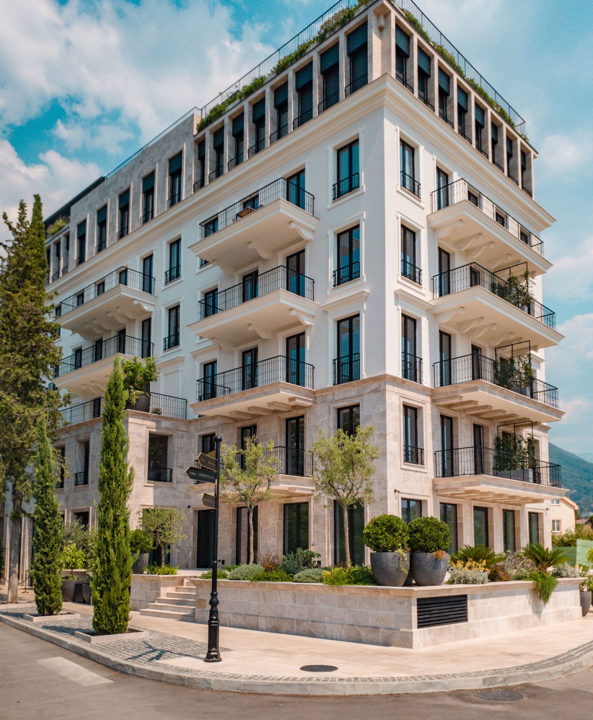 An elegant serviced-apartments building with iron balconies and cypress trees